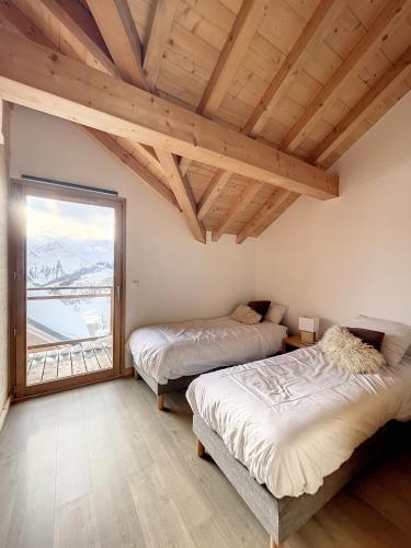two beds in a room with a large window at Chalet L'Argentière in La Toussuire