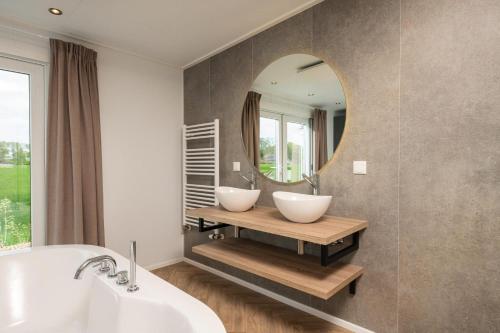 een badkamer met een bad, een wastafel en een spiegel bij Panorama lodge with jacuzzi 2 p. in Rijssen