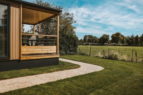 a house with a porch and a grassy field at 4-persoons Tiny Lodge in Voorthuizen