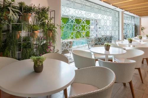 a restaurant with white tables and chairs and plants at Catalonia Giralda in Seville