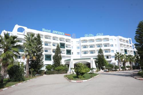 a large white hotel with palm trees in front of it at Hotel Jinene Resort in Sousse