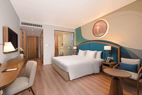 a bedroom with a white bed and a desk and a table at Wyndham Garden Sonasea Van Don in Cái Rồng