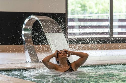 une femme dans une piscine sous une fontaine dans l'établissement Zenitude Hotel la Valadiere, Ascend Hotel Collection, à Montpellier