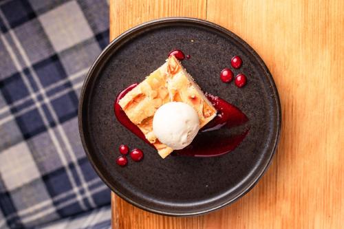 a black plate with a piece of food with ice cream at The Bell Inn, Stilton, Cambridgeshire - The Coaching Inn Group in Peterborough
