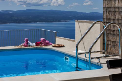 three dolls sitting on the edge of a swimming pool at Holiday home Marta with heated pool,grill,sea view in Bast