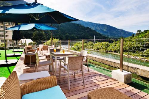 a wooden deck with chairs and tables and an umbrella at Kurobe UnazukiOnsen Togen in Kurobe