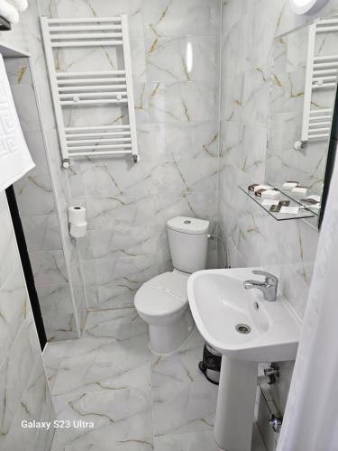 a white bathroom with a toilet and a sink at Pensiunea Minerva in Bistriţa