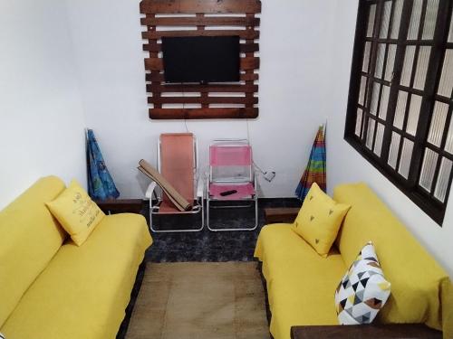 a living room with two yellow couches and a flat screen tv at Acomodações Casa 2 in Cananéia