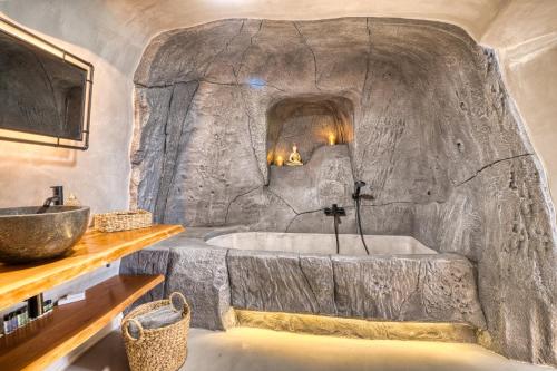 Baño cueva de piedra con bañera y lavamanos en La Ponta Apartments en Akrotiri