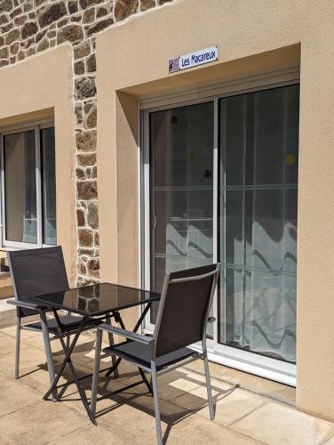 Deux chaises et une table en verre devant un bâtiment dans l'établissement Appart' avec grande terrasse vue mer -50m plage et du sentier de randonnée, à Planguenoual
