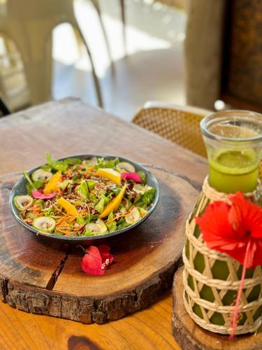 a plate of salad on a wooden table with a drink at Pousada Alto Mar in Fernando de Noronha