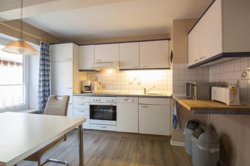 une cuisine avec des placards blancs et une table. dans l'établissement Appartement in Pellworm mit Garten, Terrasse und Grill, à Pellworm