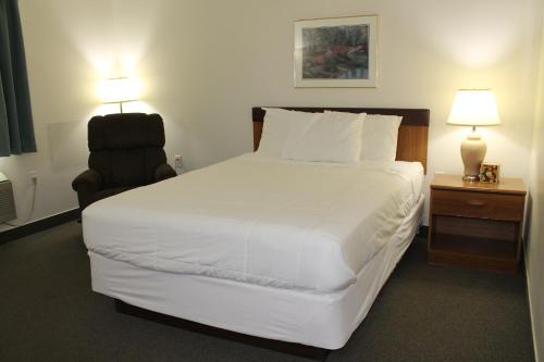 ein Schlafzimmer mit einem großen weißen Bett und einem Stuhl in der Unterkunft American Host Inn in Hart