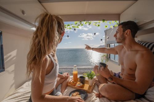 un hombre y una mujer sentados en una cama mirando por una ventana al océano en Beautiful Campervan (Mallorca), en Sant Francesc