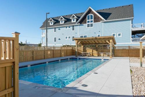 a swimming pool in front of a house with a wooden fence at FF215 First Flight Retreat 215 in Kill Devil Hills