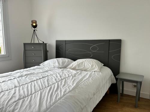 a bedroom with a white bed with a black headboard and a table at 302 - Bel appartement rénové en centre de FREHEL in Frehel