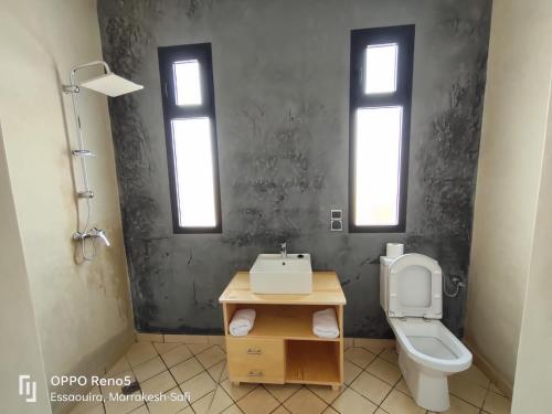 a bathroom with a toilet and a sink and two windows at Villa Tazerzit comfort et hospitalité in Essaouira