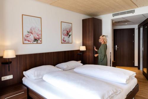 a woman standing next to a bed in a room at eduCARE Hotel in Treffen