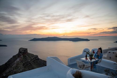 a group of people sitting at a table on a cliff with a sunset at Heavens Edge in Imerovigli