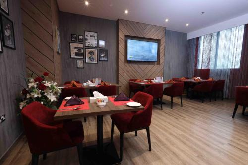 un restaurante con mesas y sillas rojas y TV en Fortis Hotel Fujairah en Fujairah