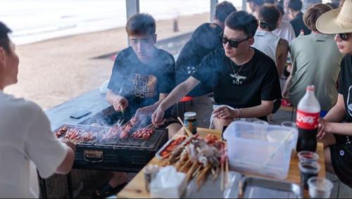 a group of people standing around a grill at Pinxiayuan Apartment in Lvcheng Resort in Zhoushan