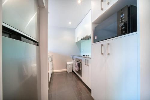 a kitchen with white cabinets and a large tv at Cosy contemporary 1BR plus sofa bed - Hosted by CanStay in Canberra