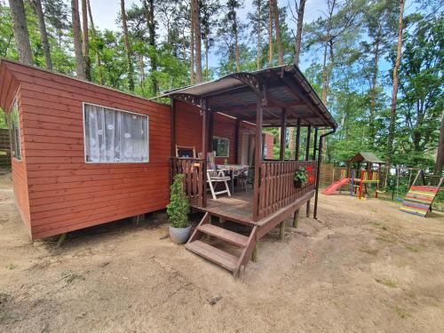 a small red cabin with a porch and a playground at POD SOSNAMI Ośrodek Wypoczynkowy Boszkowo Letnisko in Boszkowo
