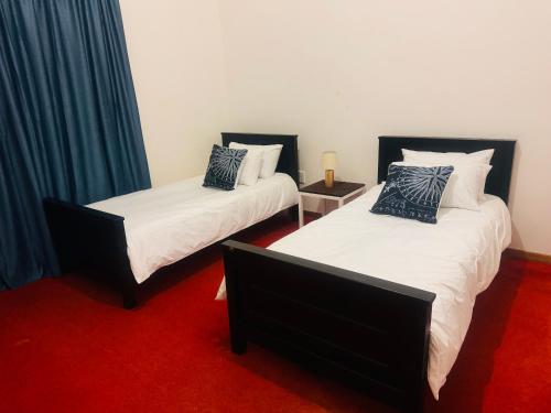 two beds in a room with a red carpet at StoneWall Villa in Mbabane