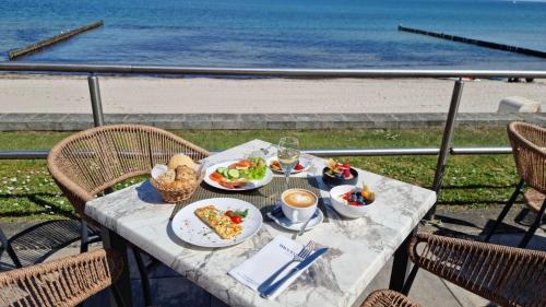 - une table avec des assiettes de nourriture et une vue sur la plage dans l'établissement meergut HOTELS, à Kühlungsborn