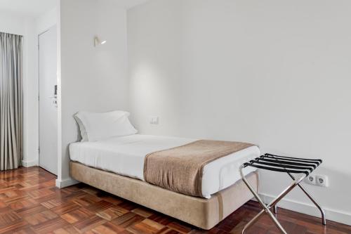 a white bedroom with a bed and a chair at Lisboa Central Park Hotel Suites & Studios in Lisbon