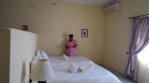 a woman in a pink dress standing next to a bed at Farmhouse Boutique Backyard Rooms in Outjo