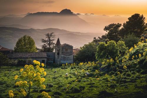 an old church in the middle of a field with flowers at Case Ruggieri Luxury apt - Don Pietro in Gratteri
