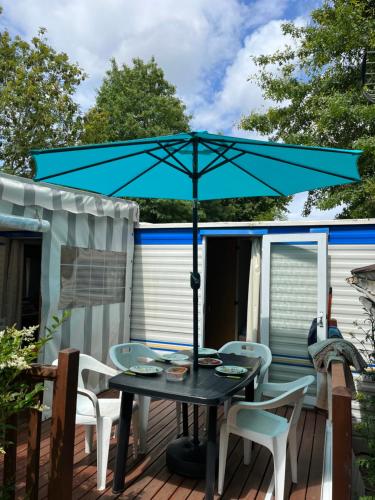 a patio table with a blue umbrella on a deck at Cosy Mobilhome in La Baule