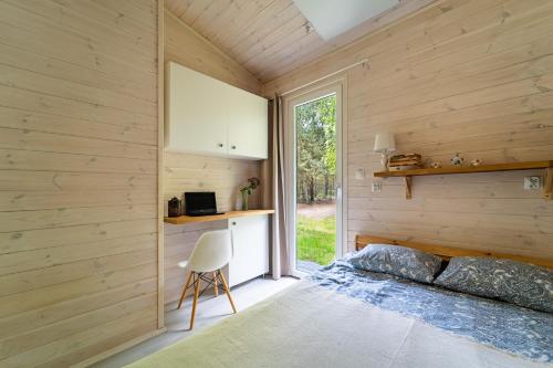 sypialnia z drewnianymi ścianami, łóżkiem i oknem w obiekcie Sosnowy Raj domki nad Wkrą w mieście Popielżyn Dolny