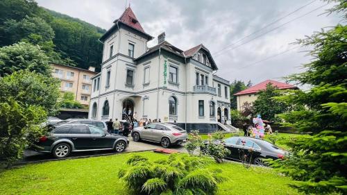 a large white house with cars parked in front of it at Vila Themis in Călimăneşti