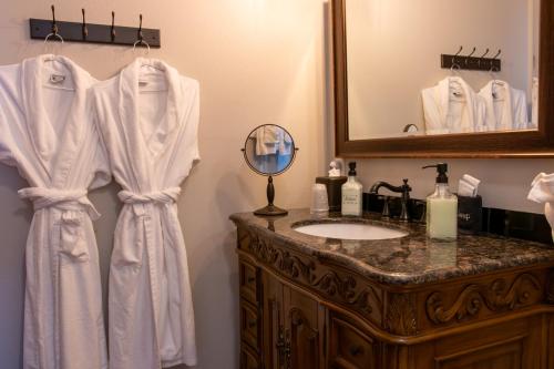 a bathroom with a sink and a vanity with white robes at The Pearl Inn Bed and Breakfast in Ilwaco