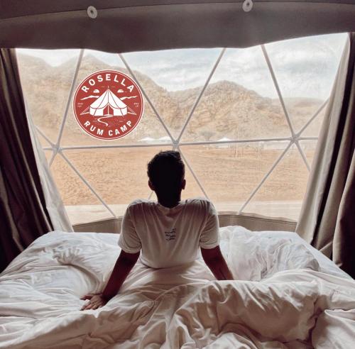 a man sitting in bed looking out of a window at Rosella rum camp in Wadi Rum