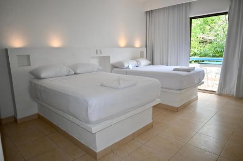 two white beds in a room with a window at Pelicano Inn Playa del Carmen - Beachfront Hotel in Playa del Carmen