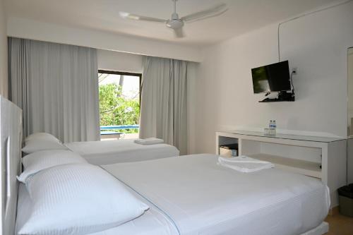 a white hotel room with two beds and a tv at Pelicano Inn Playa del Carmen - Beachfront Hotel in Playa del Carmen