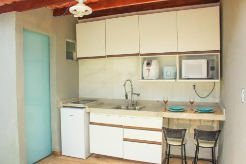 a kitchen with white cabinets and a sink and two chairs at Villa Beija-Flor2: Suíte alexa e piscina privativa in Japaratinga