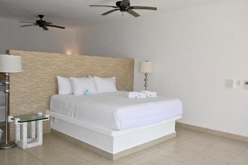 a bedroom with a white bed with a ceiling fan at Pelicano Inn Playa del Carmen - Beachfront Hotel in Playa del Carmen