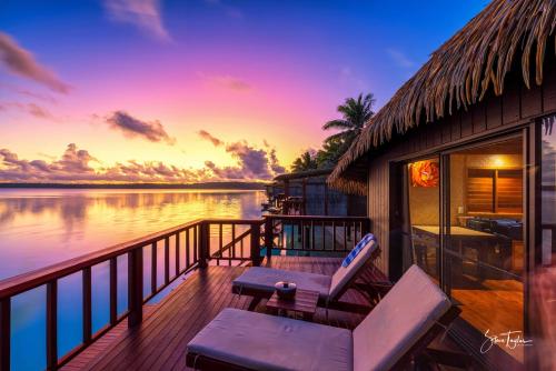 a porch with two chairs and a table and a sunset at Aitutaki Lagoon Private Island Resort (Adults Only) in Arutanga