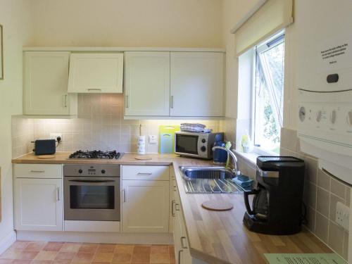 cocina con armarios blancos, fregadero y microondas en Attractive cottage in garden grounds en Jedburgh