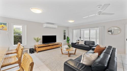 a living room with a black leather couch and a tv at Aqua Links 70 The Drive Yamba in Yamba