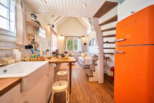 The Box House & Charming Private Tiny House & Pool في غوجيك: مطبخ برتقالي وبيض مع حوض وغرفة معيشة
