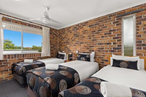 a bedroom with three beds and a brick wall at Toowong Villas in Brisbane