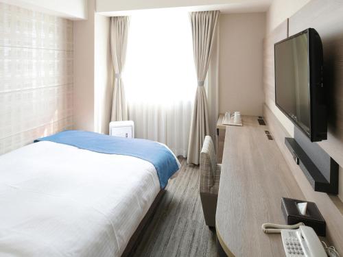 a hotel room with a bed and a flat screen tv at Vessel Inn Shigamoriyama Station in Moriyama