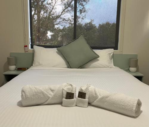 a bed with two towels and two shoes on it at Diamond Beach Holiday Park in Diamond Beach
