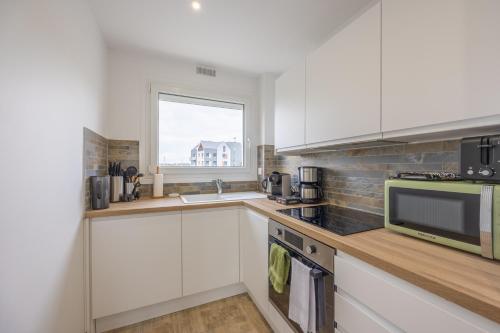 d'une cuisine avec des placards blancs, un four micro-ondes et une fenêtre. dans l'établissement La Vigie des Ours - Appt proche de la plage, à Courseulles-sur-Mer