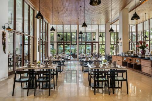 a dining room with tables and chairs and windows at Royal Tulip Springhill Resort Jimbaran in Jimbaran